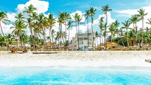 A beach resort with palm trees, a pool, and beach umbrellas. - Punta Cana Ocean View Penthouse - The Best Dominican Ocean View (Punta Cana)