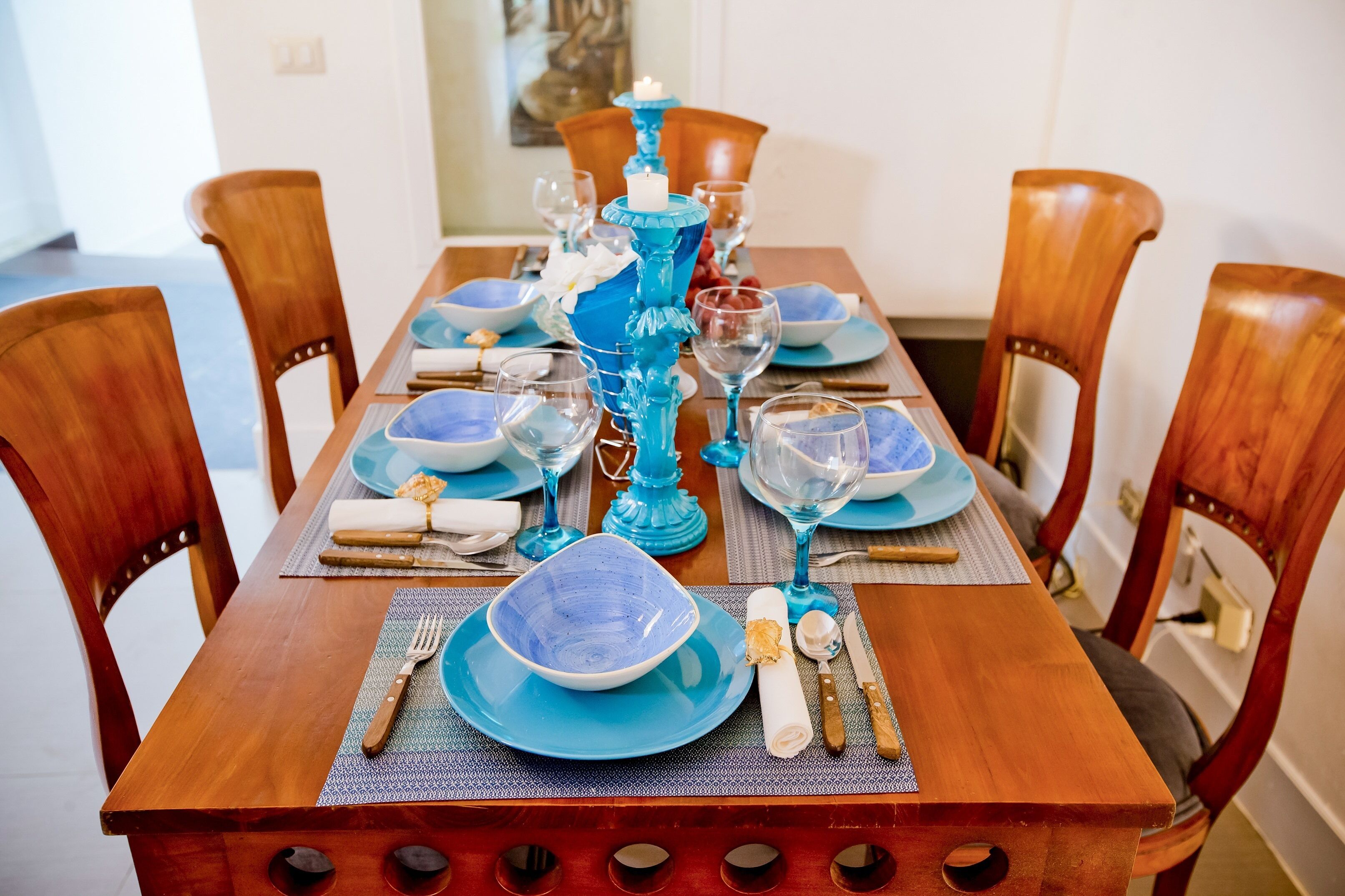A dining table set with blue plates, glasses, and a blue centerpiece.