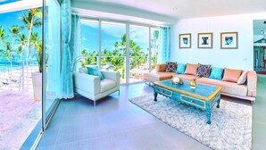A modern living room with a large glass door leading to a balcony, a beige sofa, a coffee table, and framed pictures on the wall. - Punta Cana Ocean View Penthouse - The Best Dominican Ocean View (Punta Cana)