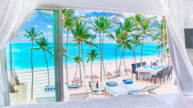 A balcony with a view of a beach and ocean, featuring a dining table and lounge chairs. - Punta Cana Ocean View Penthouse - The Best Dominican Ocean View (Punta Cana)
