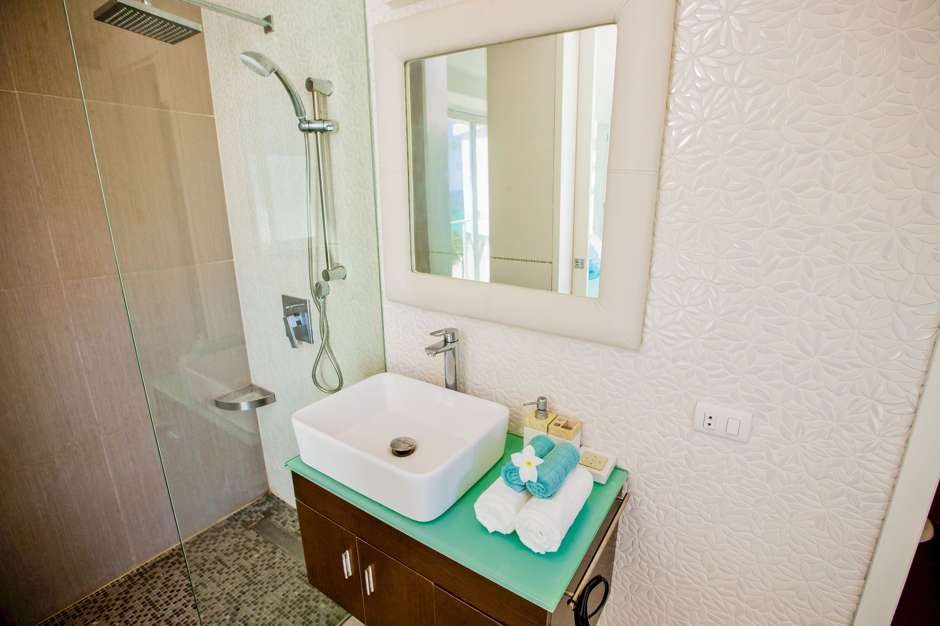 Een badkamer met een glazen douchecabine, een witte wastafel, een spiegel en een groen aanrecht.