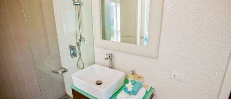 Een badkamer met een glazen douchecabine, een witte wastafel, een spiegel en een groen aanrecht.