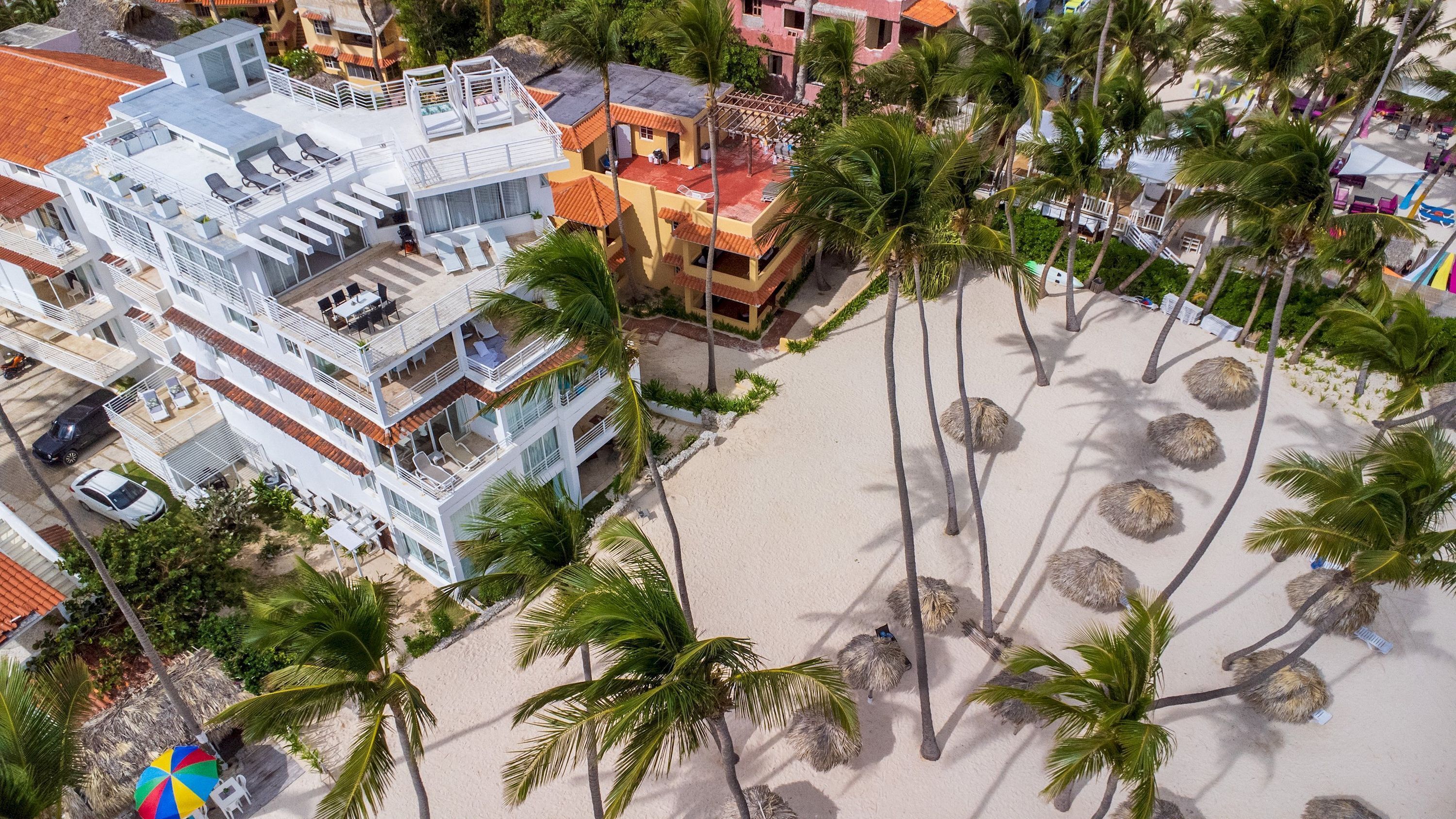 Un hôtel à plusieurs étages doté de balcons, une zone de plage bordée de palmiers et une plage de sable.