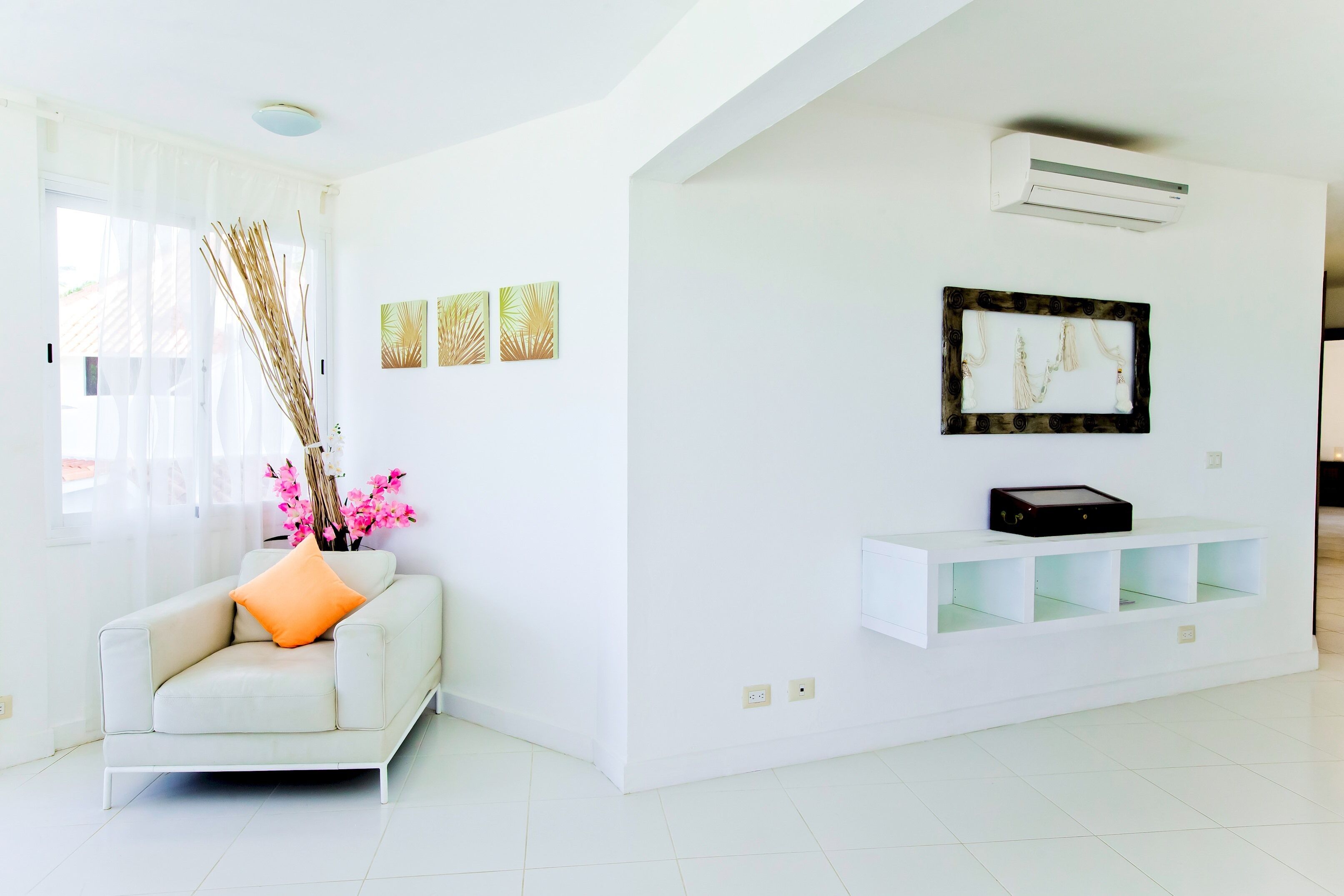 Un salón moderno con un sofá blanco, un jarrón con plantas secas y un cuadro en la pared.