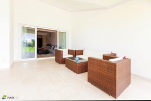 A spacious living area with a modern design, featuring a large sliding glass door leading to a balcony, a comfortable seating arrangement, and a glass coffee table.