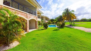 A two-story house with a swimming pool, surrounded by a well-maintained lawn and palm trees. - Punta Cana Condo With Swimming Pool - Bavaro Condo Cocotal Sanitized (Punta Cana)
