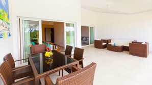 A modern living room with a glass dining table, wicker furniture, and a view of a balcony. - Punta Cana Condo With Swimming Pool - Bavaro Condo Cocotal Sanitized (Punta Cana)