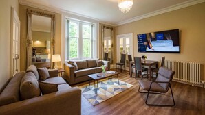 A spacious living room with a sofa set, a coffee table, and a TV mounted on the wall. - Rosedene Highland House - Emperor Apartment 7 (Inverness)