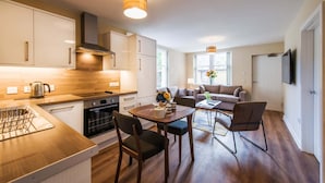 Une cuisine moderne avec des meubles en bois, un coin repas avec une table et des chaises, et un salon avec un canapé et un téléviseur.