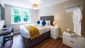 Une chambre d’hôtel avec un lit, des tables de chevet, un bureau, une fenêtre donnant sur un espace verdoyant et un peignoir suspendu à un porte-manteau.