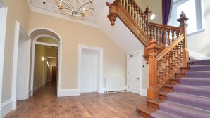 A spacious hallway with wooden flooring, a wooden staircase with purple carpeted steps, and a white radiator.