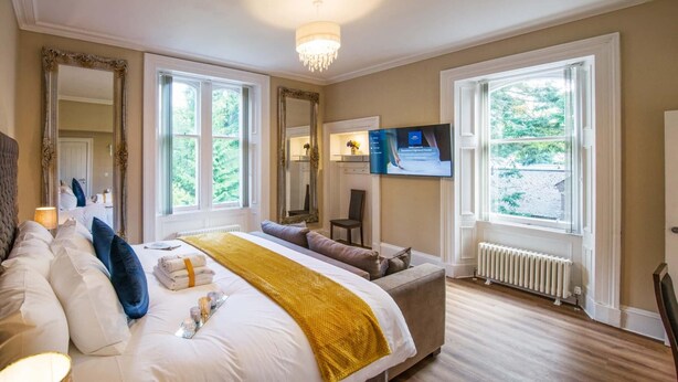 Hotellihuone, jossa on suuri sänky, sohva, televisio ja näkymä ulos.