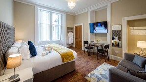 A hotel room with a large bed, a desk, a television, and a seating area. - Rosedene Highland House - Emperor Studio Apartment 3 (Inverness)