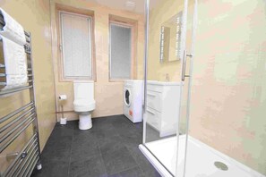 A bathroom with a toilet, washing machine, and a glass shower enclosure. - Rosedene Highland House - Emperor Studio Apartment 3 (Inverness)