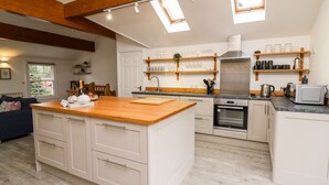 A modern kitchen with a central island, wooden beams, skylights, and built-in appliances. - Bridgend Cottages (Llandrindod Wells)