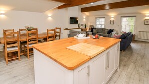 A spacious kitchen with wooden beams, a dining area with chairs, a sofa, and a TV mounted on the wall. - Bridgend Cottages (Llandrindod Wells)