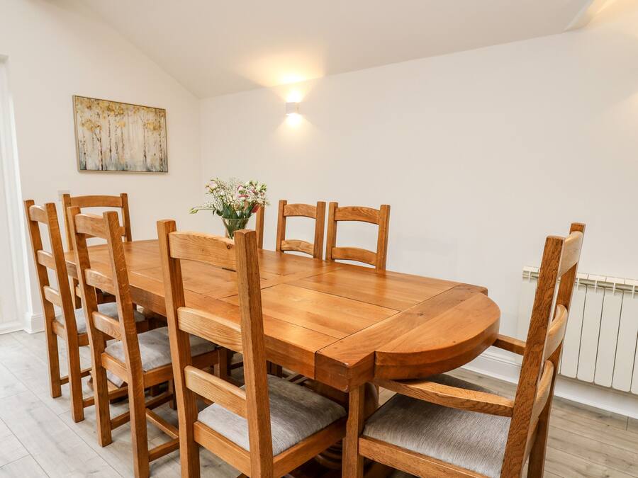 A dining table with six wooden chairs, a vase with flowers, and a painting on the wall.