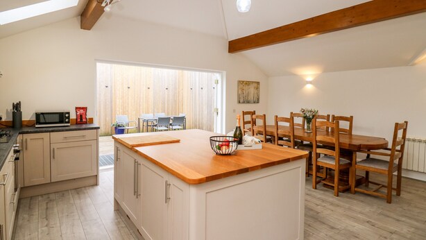 A modern kitchen with a central island, wooden dining table, and chairs. - Bridgend Cottages (Llandrindod Wells)