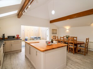 A modern kitchen with a central island, wooden dining table, and chairs. - Bridgend Cottages (Llandrindod Wells)