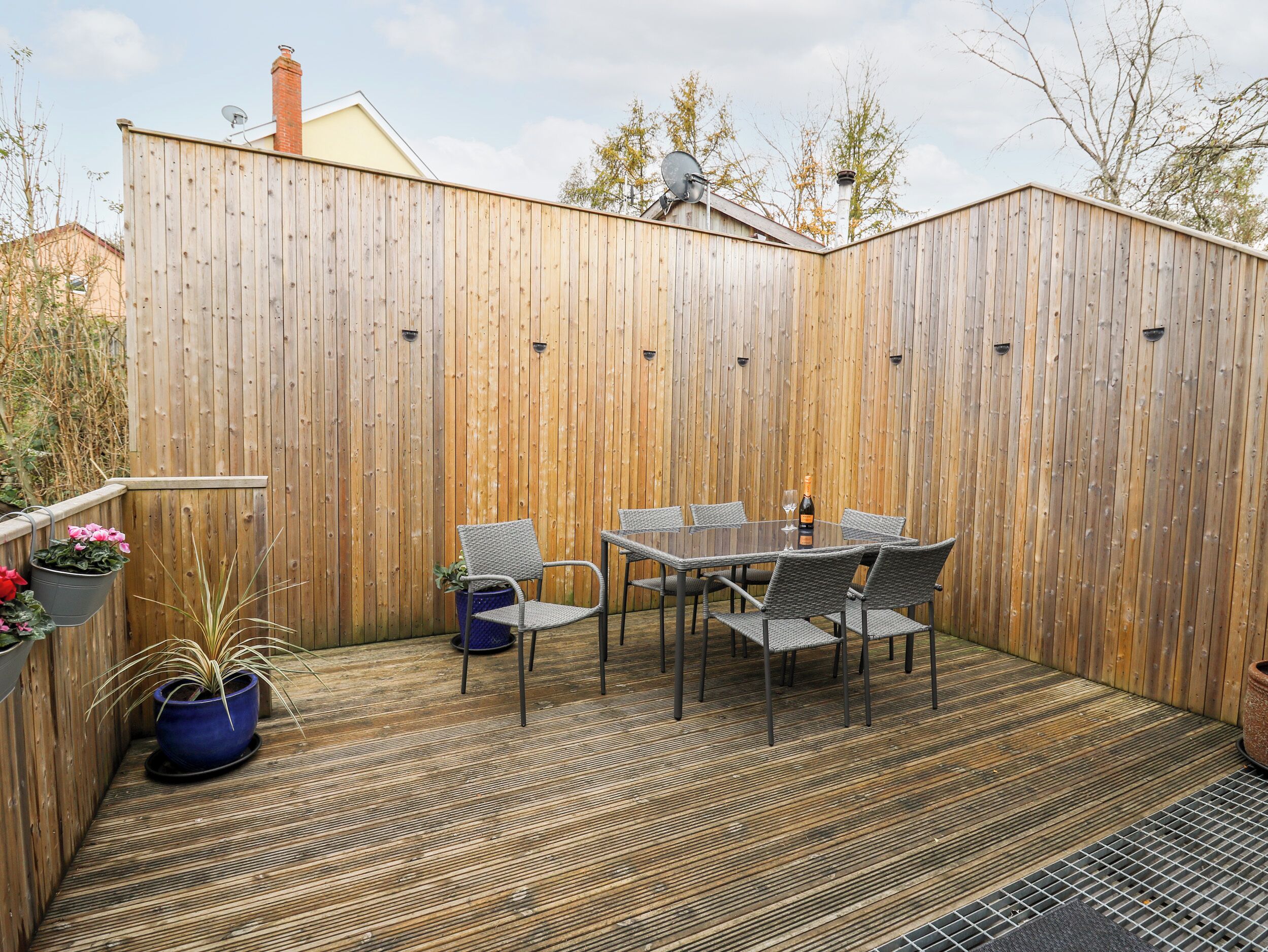 A wooden deck with a glass table and chairs, surrounded by a wooden fence.