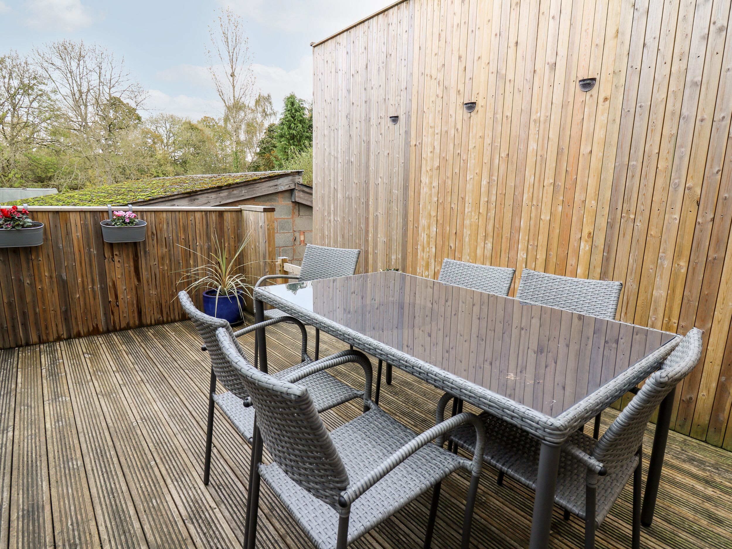 Una terraza de madera con una mesa de vidrio y sillas de mimbre.