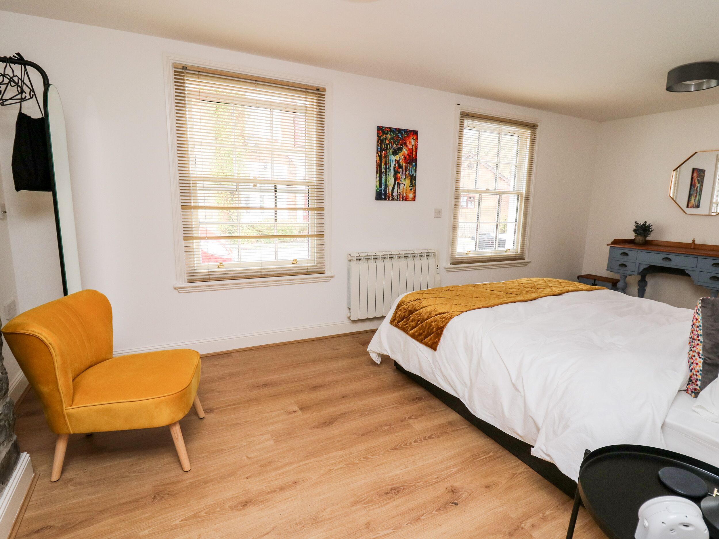 Ein Schlafzimmer mit Bett, Stuhl, Schreibtisch und zwei Fenstern mit Jalousien.