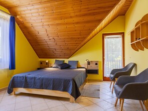Ein Schlafzimmer mit Holzboden, einem Bett mit blauer Bettdecke, zwei Nachttischen, einem Sessel und einem Fenster mit blauen Vorhängen.