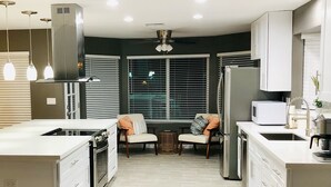 A modern kitchen with a central island, built-in appliances, pendant lighting, and a view through large windows. - Spacious Home, Private Pool, minutes to Spring Training, and Cardinal Stadium (Peoria)