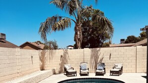 A swimming pool with clear blue water, surrounded by a beige brick wall, and three lounge chairs with cushions. - Spacious Home, Private Pool, minutes to Spring Training, and Cardinal Stadium (Peoria)