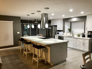 A modern kitchen with a central island, bar stools, stainless steel appliances, and pendant lighting. - Spacious Home, Private Pool, minutes to Spring Training, and Cardinal Stadium (Peoria)