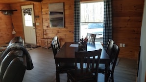 A wooden cabin interior with a dining table, chairs, a bench, a fireplace, and a view of a car through the window. - Mountain View Cabin (Lovell)