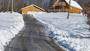 A wooden cabin with a covered porch and a garage, surrounded by snow-covered ground and leafless trees. - Mountain View Cabin (Lovell)
