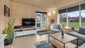 Ett modernt vardagsrum med en platt-TV, en soffa, ett soffbord och ett stort fönster med utsikt över trädgården.