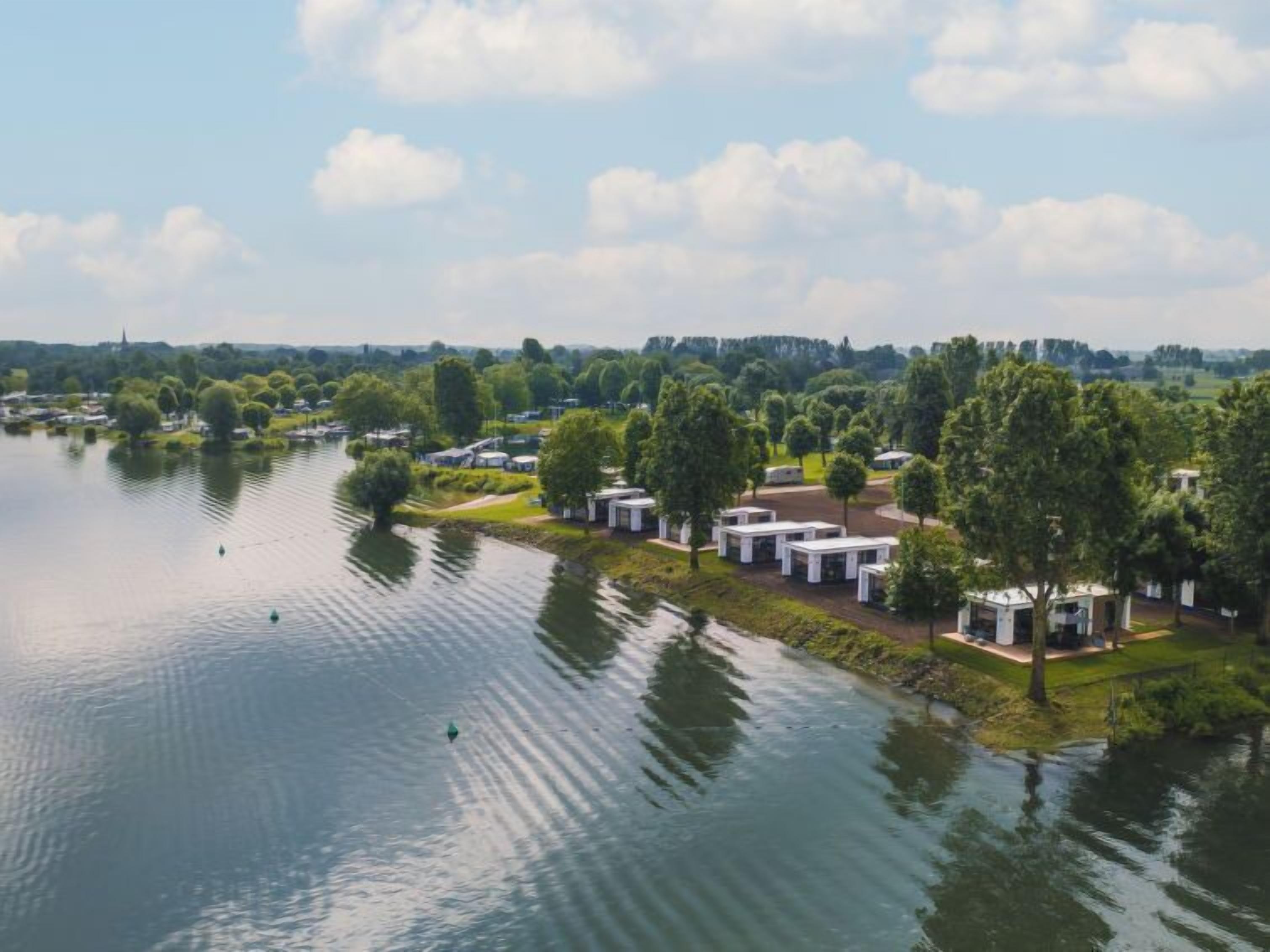 A lakeside property with multiple white cabins, surrounded by lush greenery and trees.