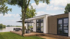 Ein modernes Haus mit einer Terrasse, einem Grill und Blick auf einen See.