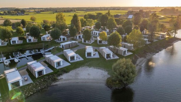 Ein Caravanpark am Seeufer mit kompakten, modernen Hütten und einem ruhigen Wasserspiegel.