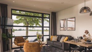 Ein modernes Wohnzimmer mit großem Fenster mit Blick auf ein Gewässer, einer Couch, einem Couchtisch und einem Essbereich mit Stühlen.