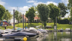 Ein Yachthafen mit vertäuten Booten, ein Spielplatz und eine begrünte Fläche mit Bäumen.