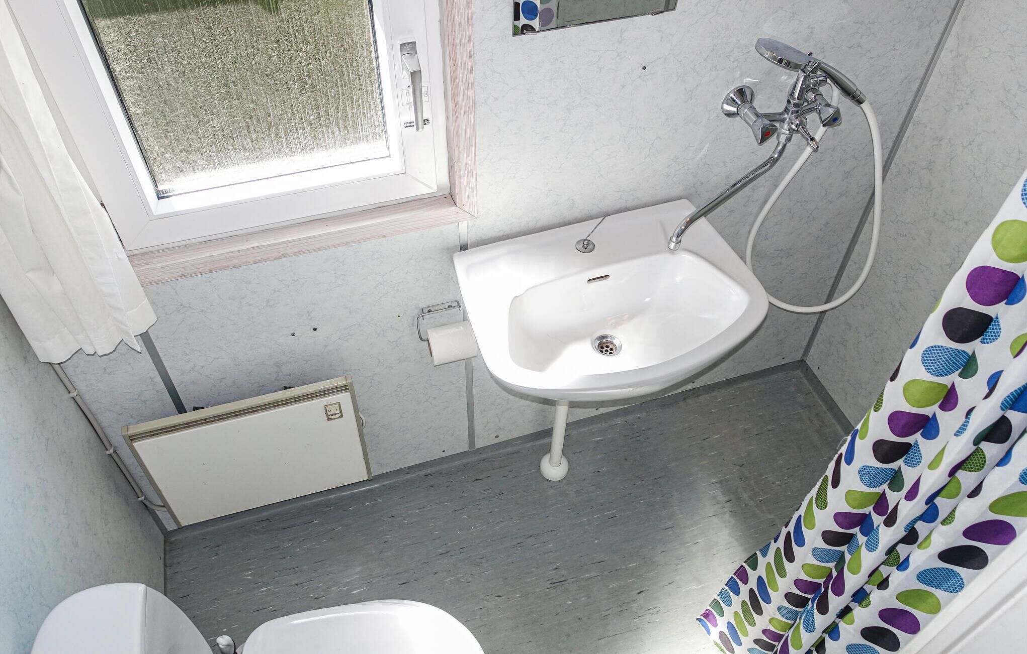 A small bathroom with a white sink, a shower, and a window.