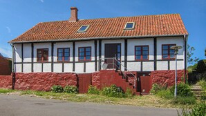 Una casa de dos pisos con techo de tejas rojas, paredes blancas y base roja.