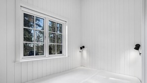 A room with white paneled walls, a large window with a view of trees, and a bed with a white bedspread. - Amazing home in Nexø with kitchen (Nexø)
