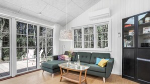 A modern living room with a green sofa, a glass coffee table, and a large window with a view of trees. - Amazing home in Nexø with kitchen (Nexø)