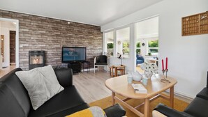 A modern living room with a stone wall, a fireplace, a television, and a dining area with a table and chairs. - Gorgeous home in Nexø with WiFi (Nexø)