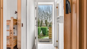 A hallway with a wooden bench, a door with a black handle, and a view of a garden with a hedge and trees.