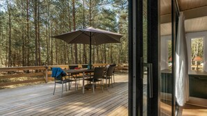 Un terrazzo in legno con tavolo e sedie, un ombrellone e vista su una foresta.