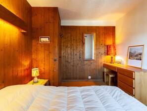 Une chambre avec des murs en bois, un lit, une table de chevet avec une lampe, une commode et un miroir.