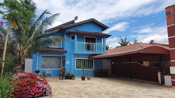 A two-story house with a blue exterior, a balcony, and a covered patio area. - Morada Lira (Bertioga)