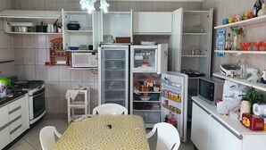 A compact kitchen with white cabinets, a microwave, a refrigerator, a gas stove, and a dining table with chairs. - Morada Lira (Bertioga)