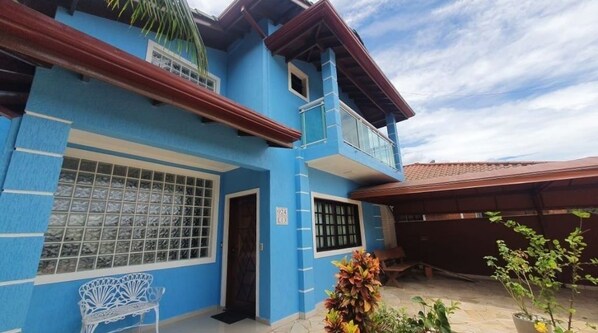 A two-story building with a blue exterior, a balcony, and a covered patio area. - Morada Lira (Bertioga)