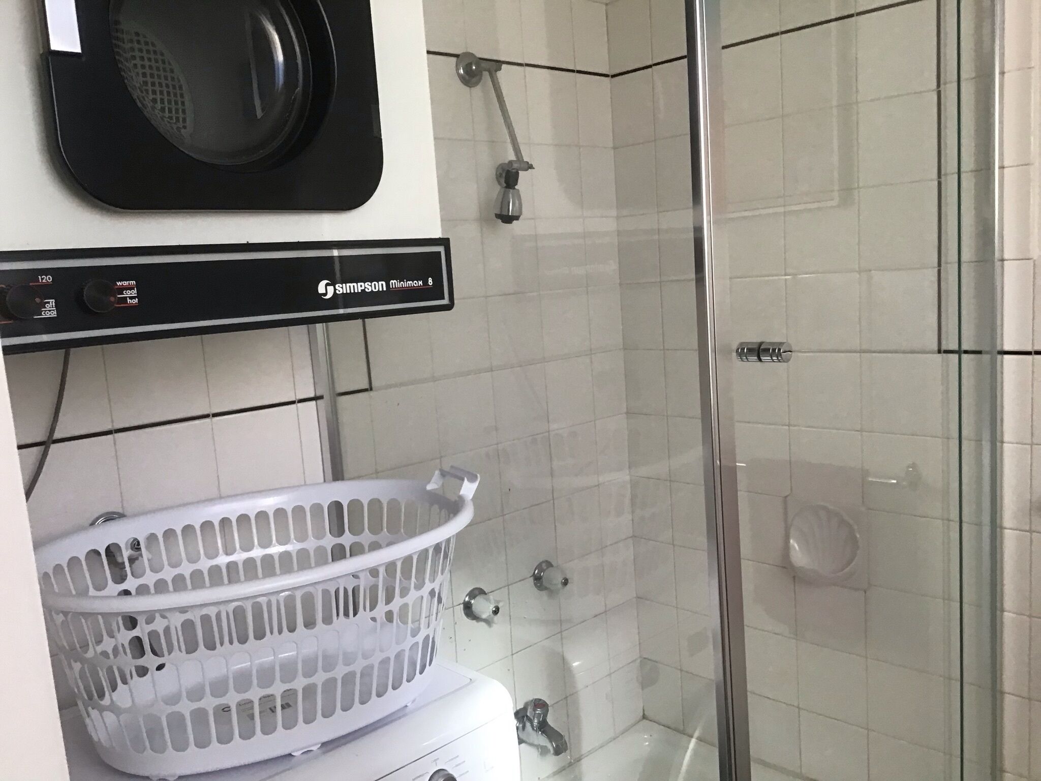 Een badkamer met een douche, een witte wasbak en een witte wasmand.